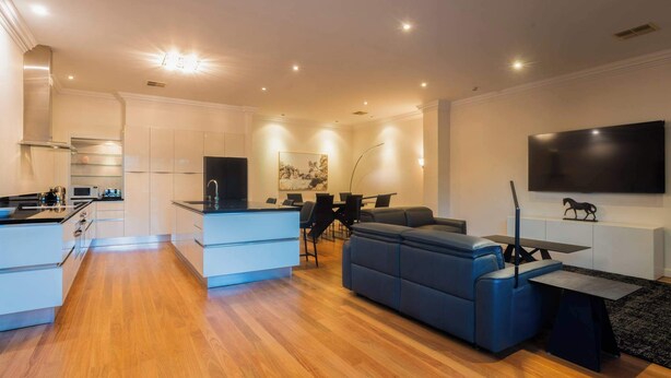 A modern living room with a sofa, a dining area, a kitchen, and a TV mounted on the wall. - Spacious 3 BDR family home with Parking and BBQ! (Perth)