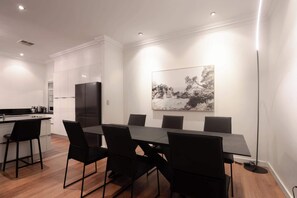 A modern dining area with a long table, black chairs, and a large black-and-white painting on the wall.