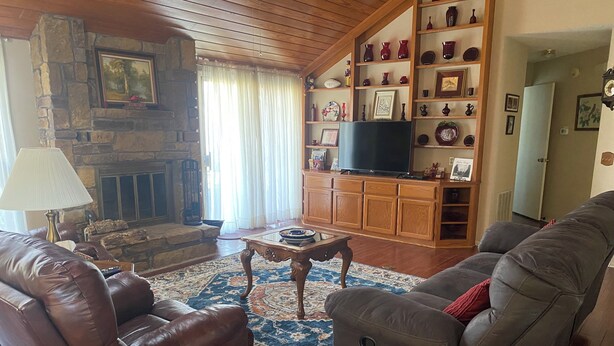 A living room with a stone fireplace, leather sofas, a television, and a bookshelf filled with decorative items.