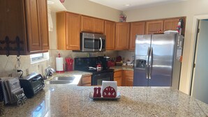 A kitchen with wooden cabinets, a stainless steel refrigerator, a microwave, and granite countertops.
