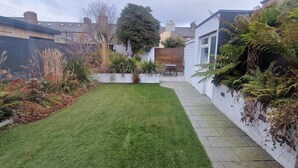 A residential garden with a well-maintained lawn, a white wall with climbing plants, and a wooden bench.