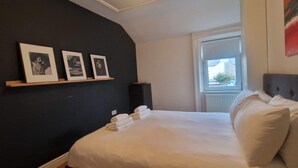 A bedroom with a bed, a dark wall, a window, and a speaker.