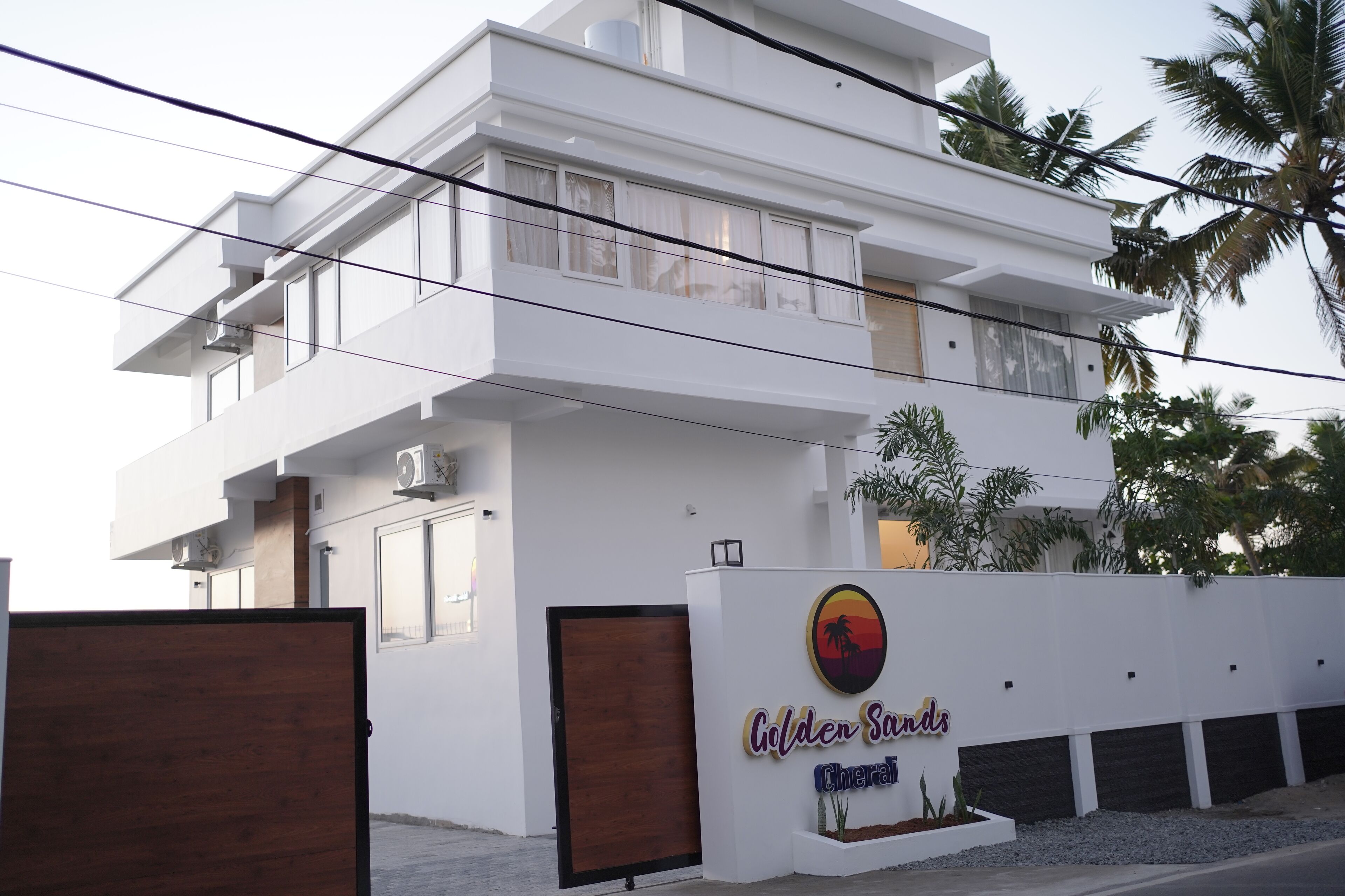 A modern two-story building with a white facade, a balcony, and a sign that reads "Golden Sands Cherazi".