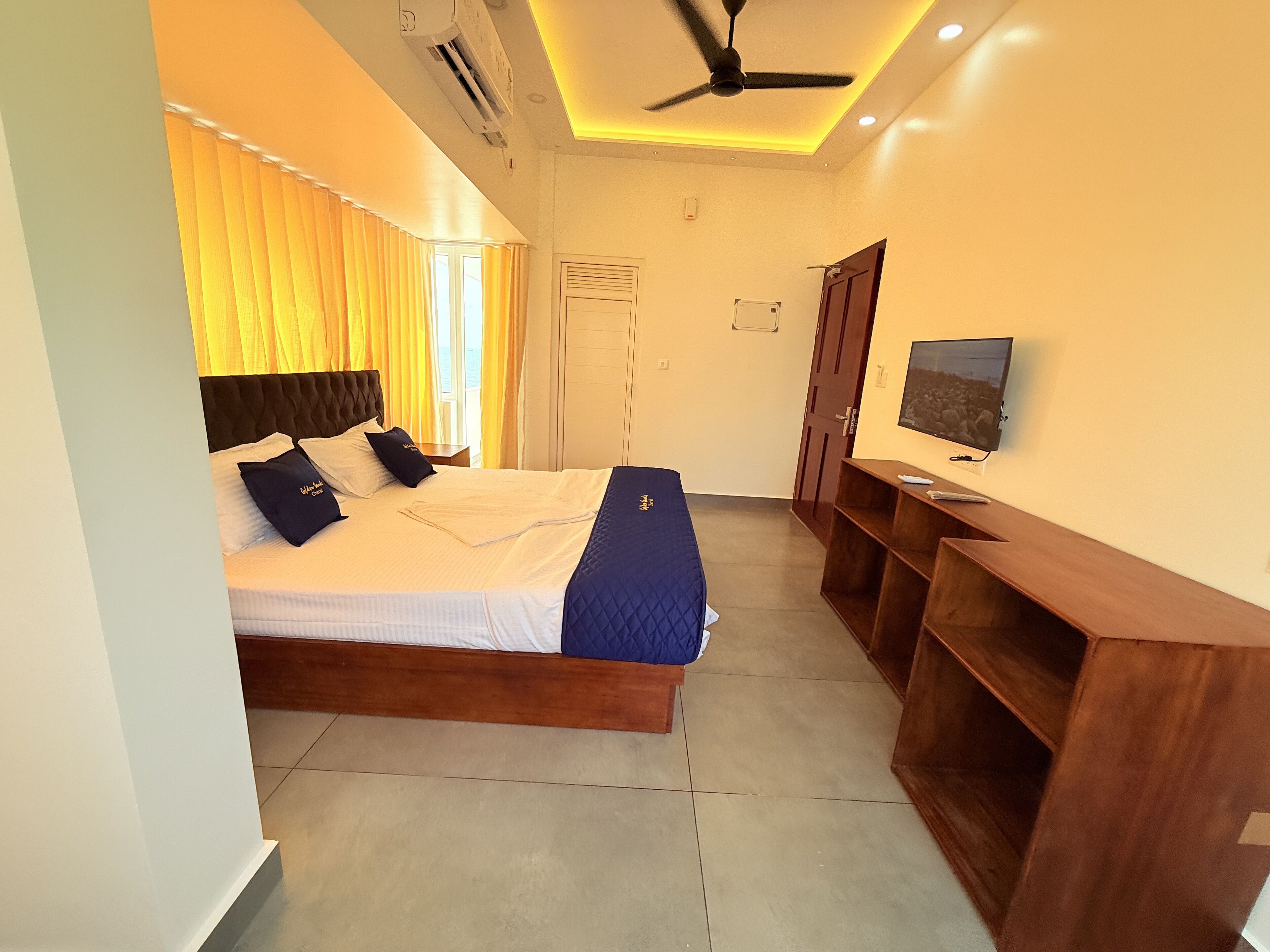 A hotel room with a bed, a TV, a ceiling fan, and a wooden desk.