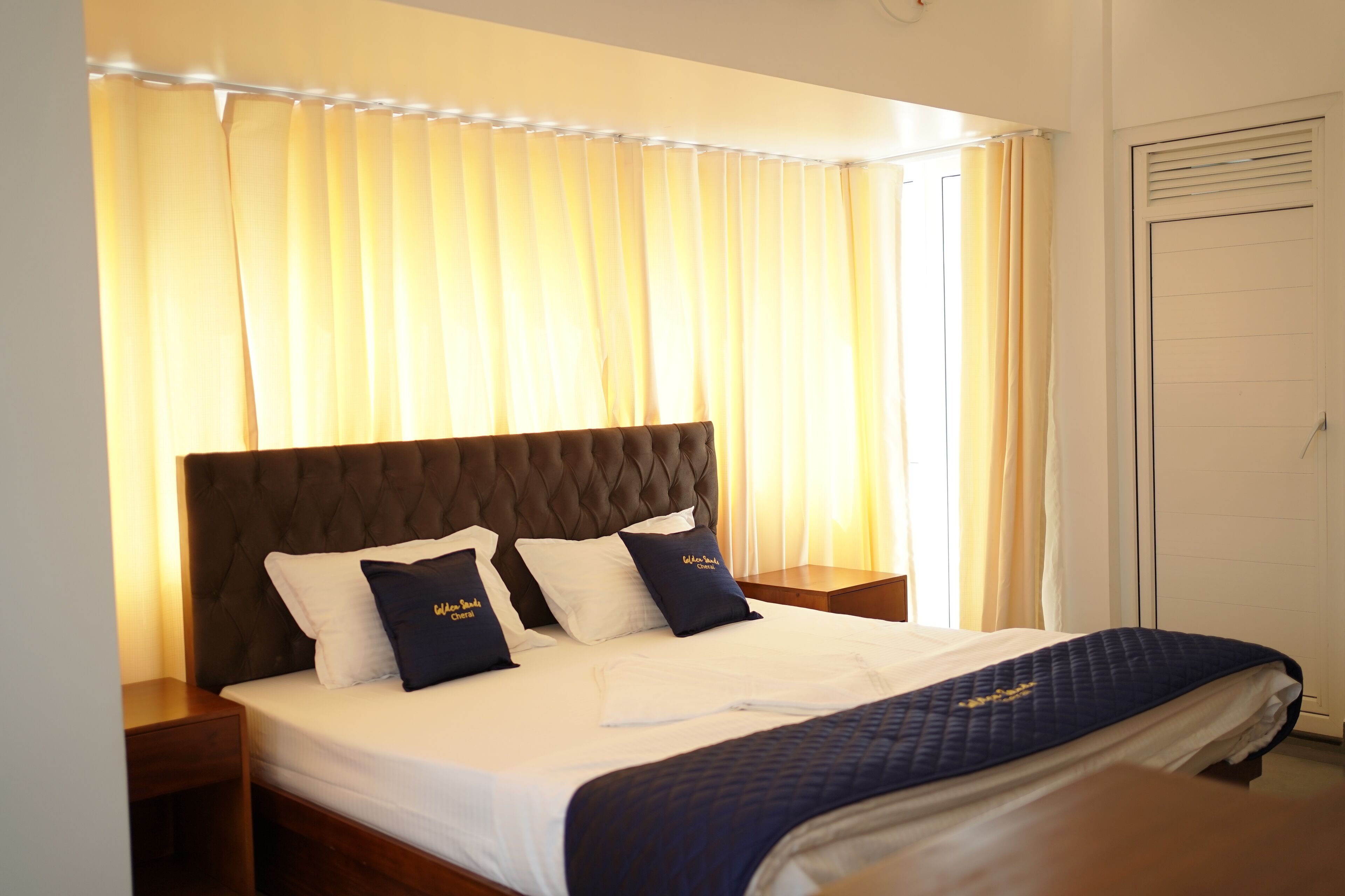 A neatly made bed with a dark headboard, white linens, and two navy pillows.