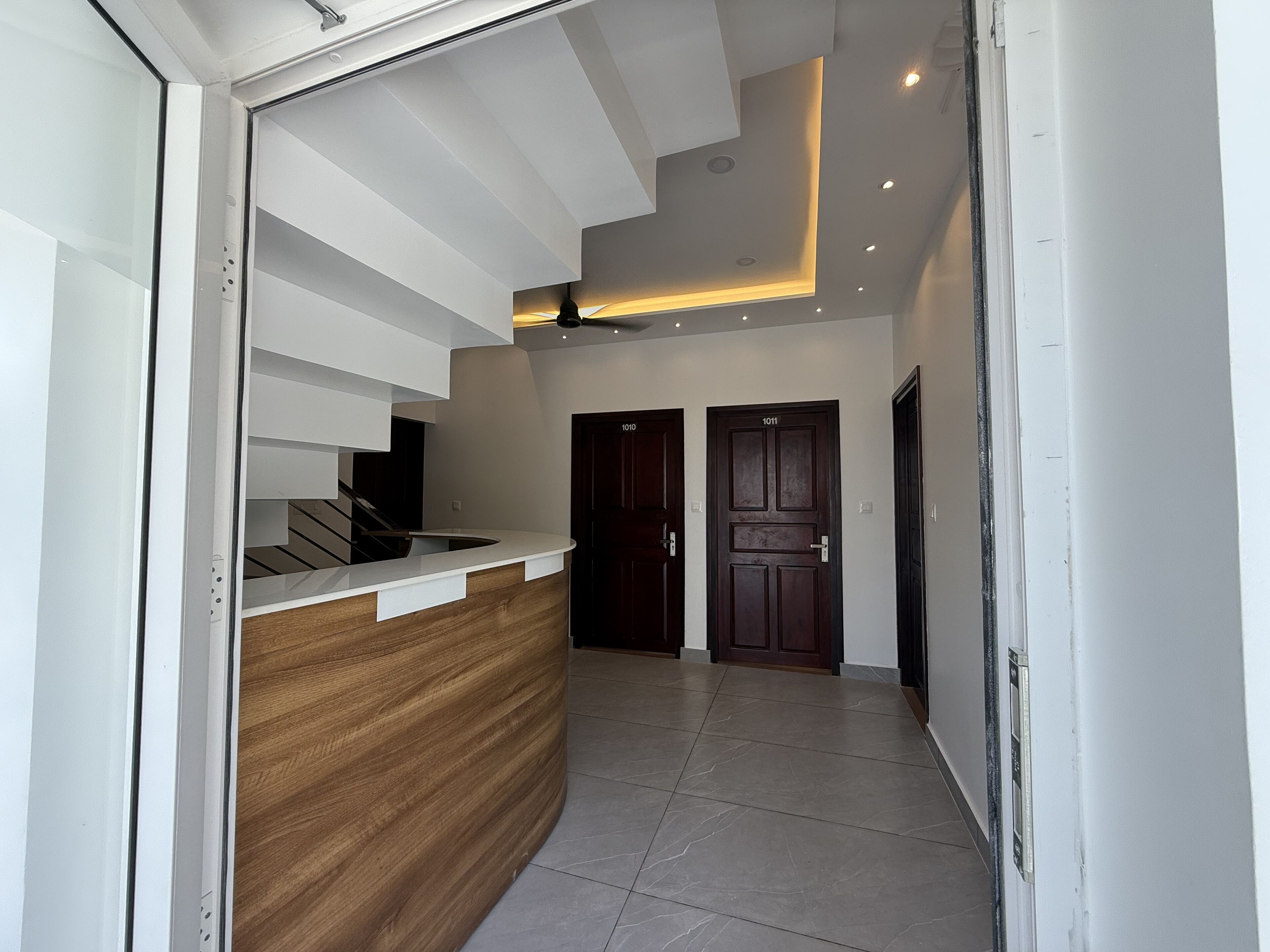 A modern reception area with a wooden reception desk, two dark wooden doors, and a ceiling with recessed lighting.