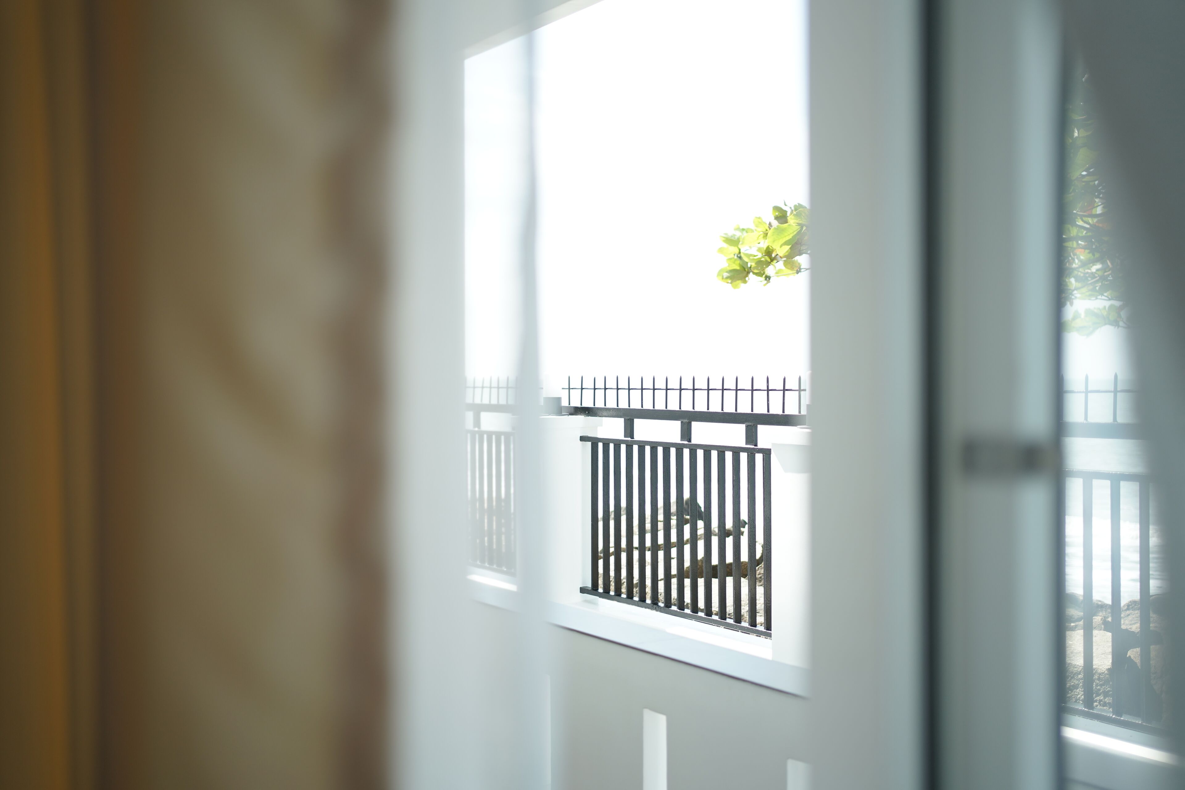 A view through a window with a metal railing, a white door frame, and a curtain partially visible on the left.