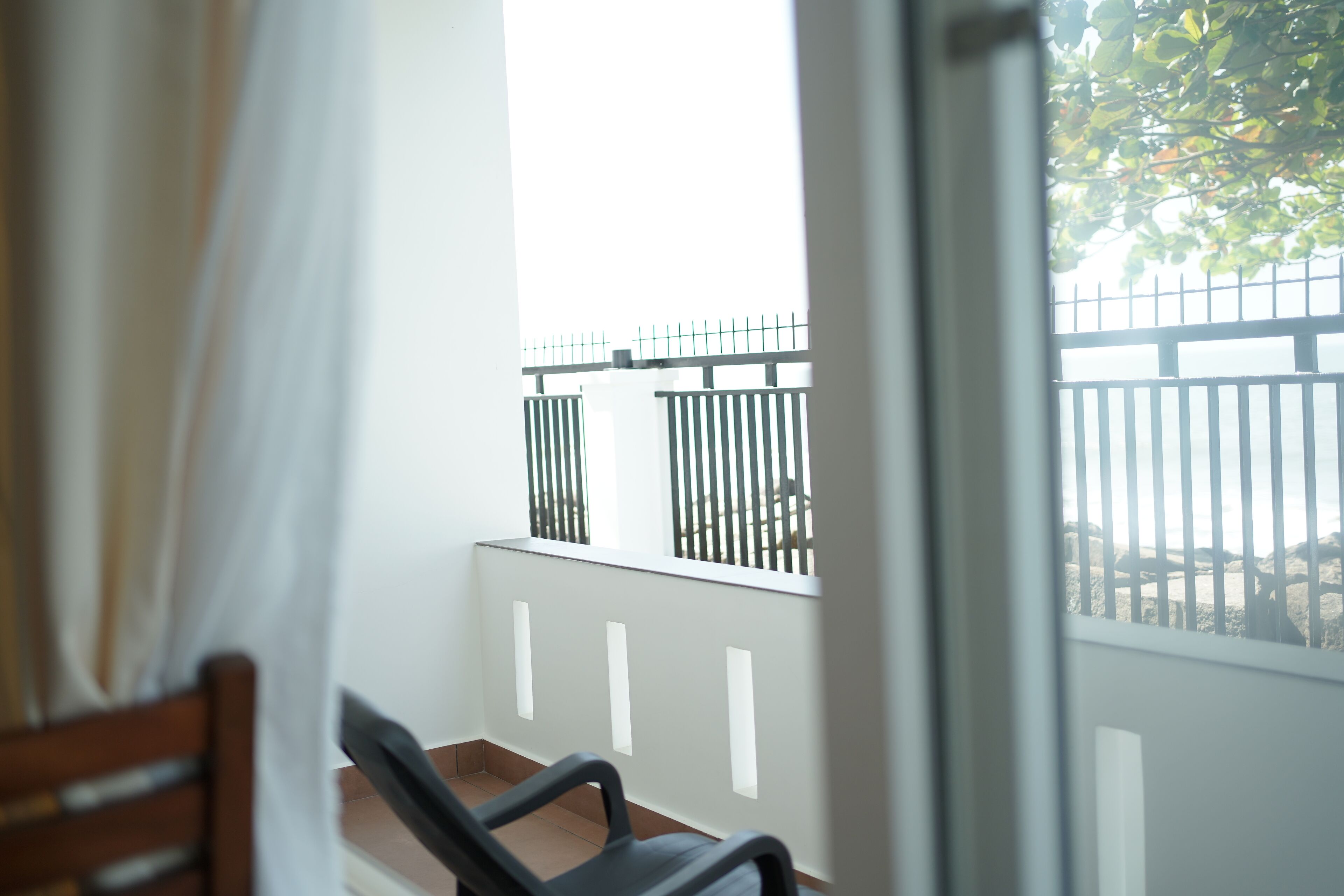 A balcony with a white railing, a wooden chair, and a view of a fence and trees.
