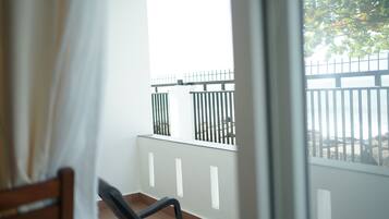 A balcony with a white railing, a wooden chair, and a view of a fence and trees.