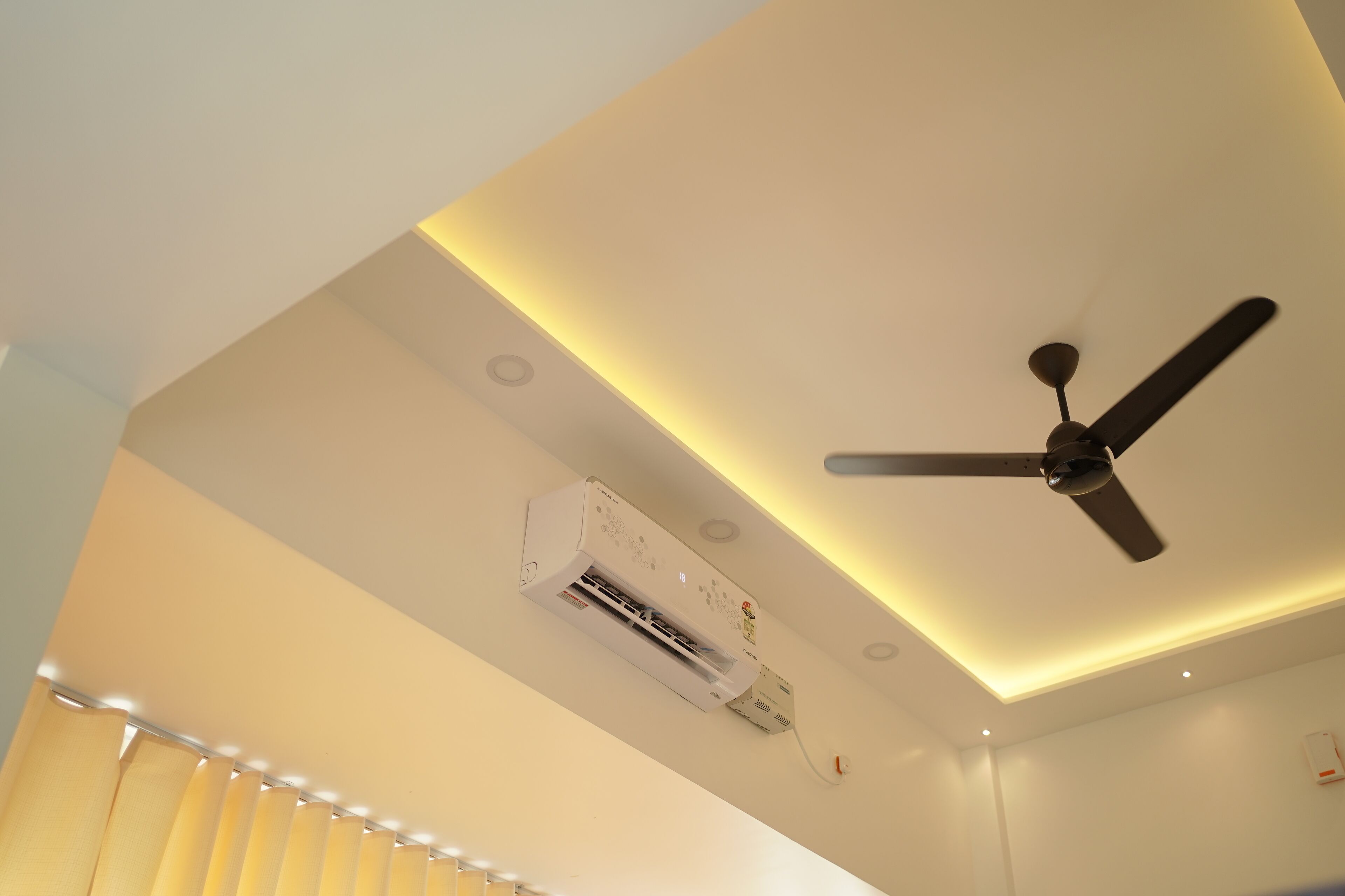 Un plafond doté d’un ventilateur de plafond, d’un appareil de climatisation, d’un éclairage encastré et d’une fenêtre avec des rideaux.