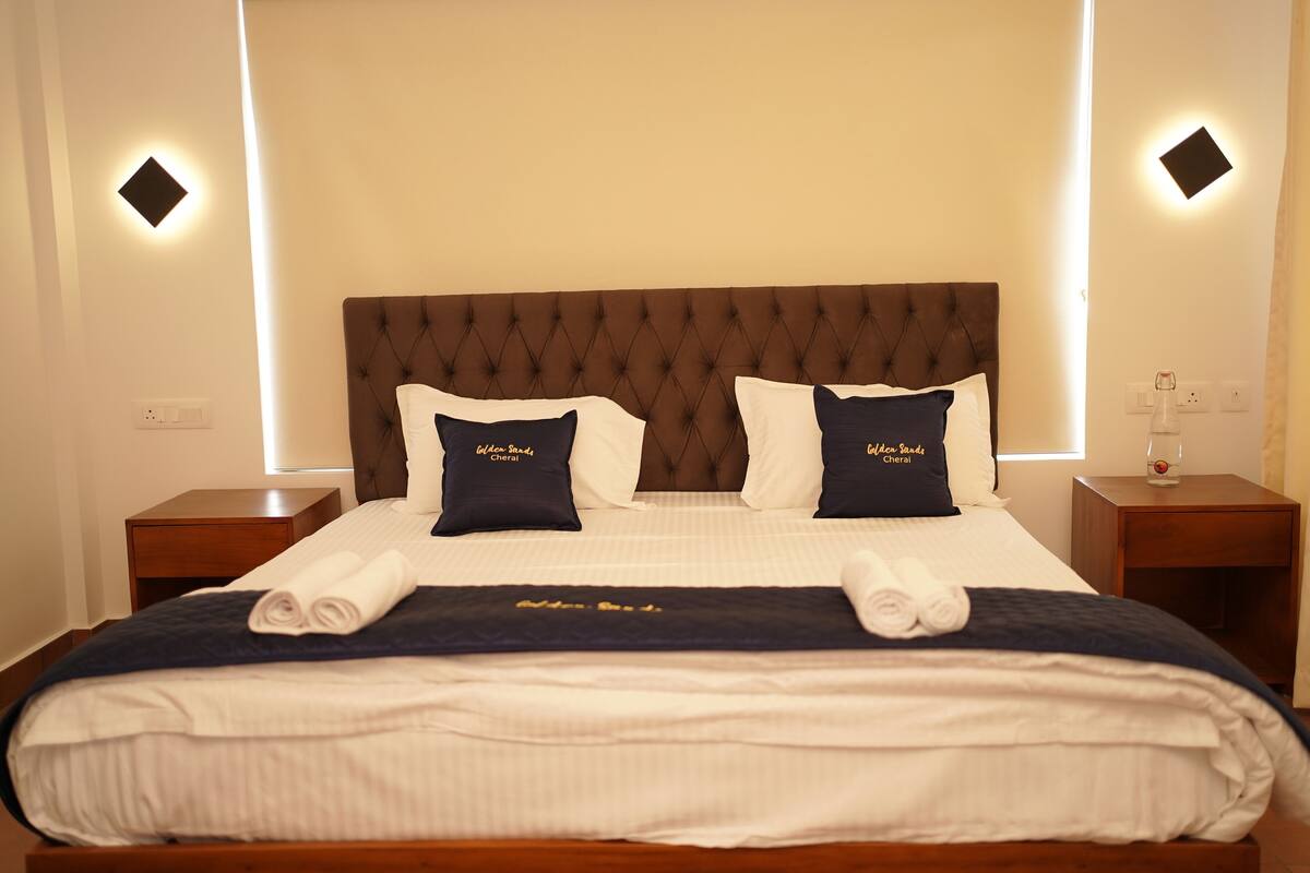 Ein ordentlich bezogenes Bett mit einer gebügelten Zirpenkopflehne, zwei Kissen mit Aufdruck und ein gefaltetes Handtuch auf dem Bett.