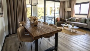 Una sala de estar moderna con una mesa de comedor de madera, sillas color beige, un sofá y vistas al exterior.