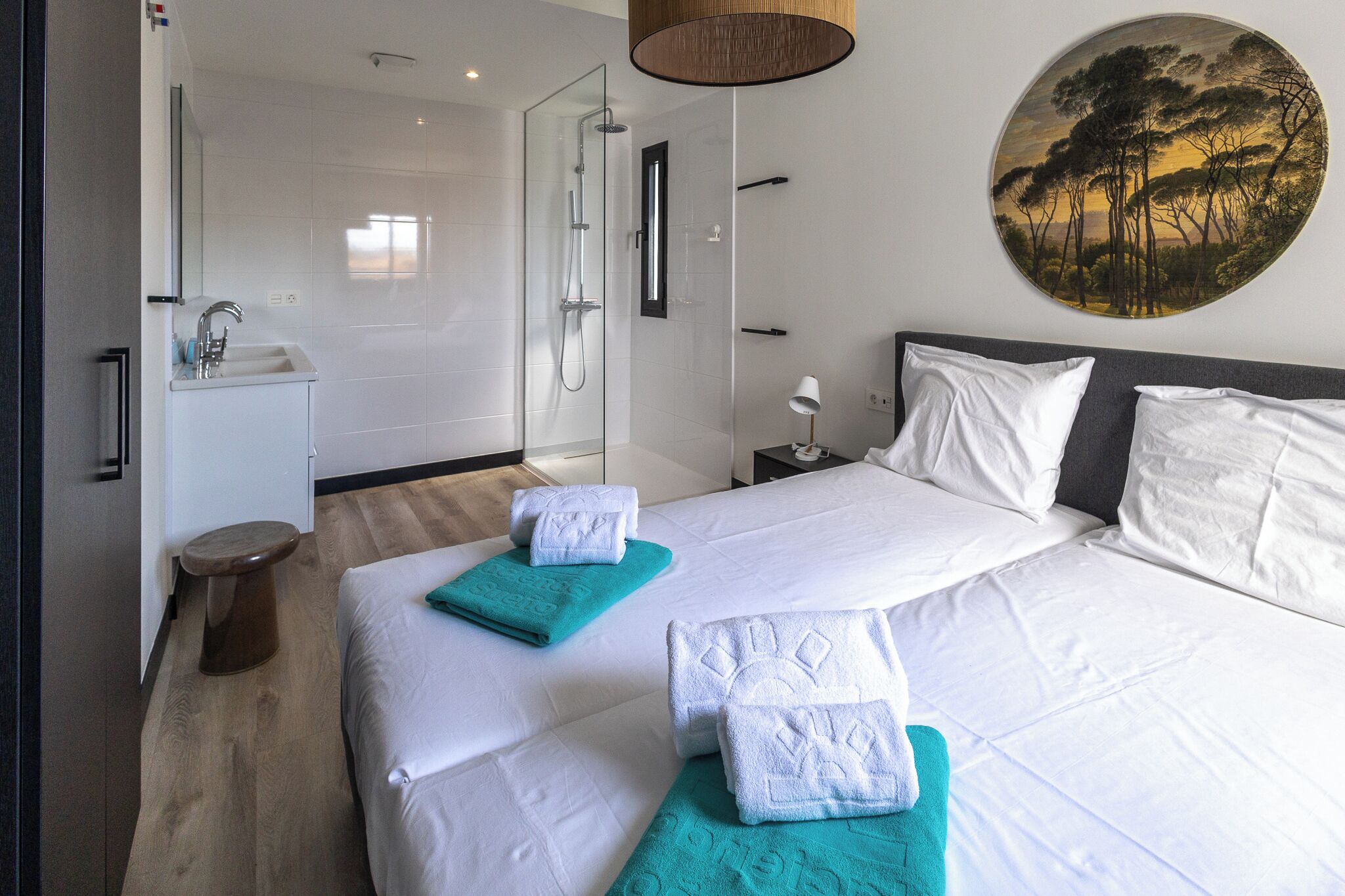 A modern hotel room with a large bed, a separate shower area, a small sink, and a round painting on the wall.