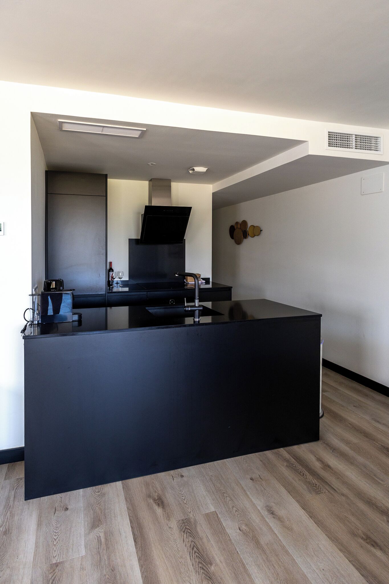 A modern kitchen with a black countertop, wooden flooring, and a built-in stove.