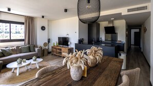 Una sala de estar moderna con una mesa de comedor de madera, sofás blancos y una cocina al fondo.