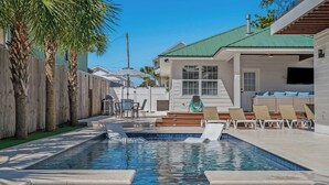 Une piscine avec un jacuzzi, des chaises longues et un espace salon couvert.