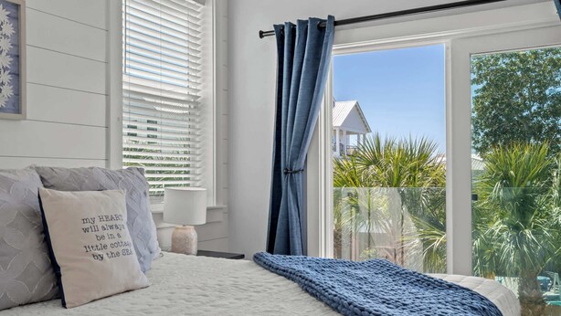 Une chambre avec un lit, une fenêtre avec des stores, une vue sur des palmiers et un balcon.