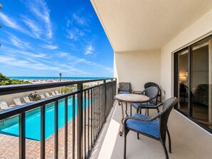 A balcony with a pool, two chairs, and a view of the ocean.