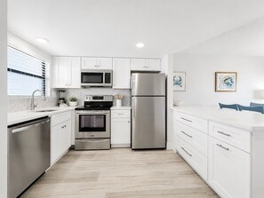 A modern kitchen with white cabinetry, stainless steel appliances, and a tiled floor.