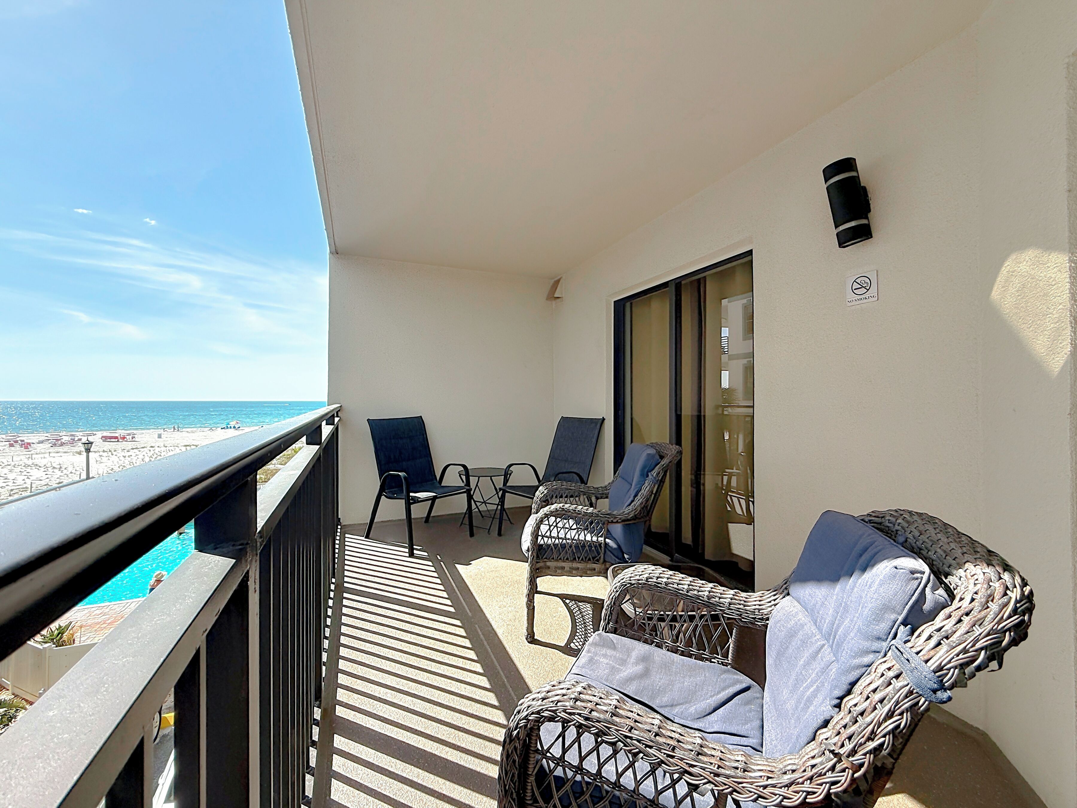 Ein Balkon mit Korbmöbeln, einer Glastür und Blick auf den Strand.