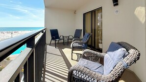 A balcony with wicker furniture, a glass door, and a view of the beach. - Coastal Beachfront Condo | Pool & Jacuzzi (St. Pete Beach)