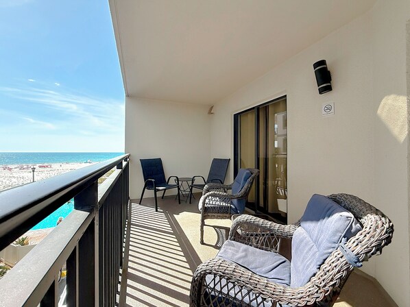 A balcony with wicker furniture, a glass door, and a view of the beach.