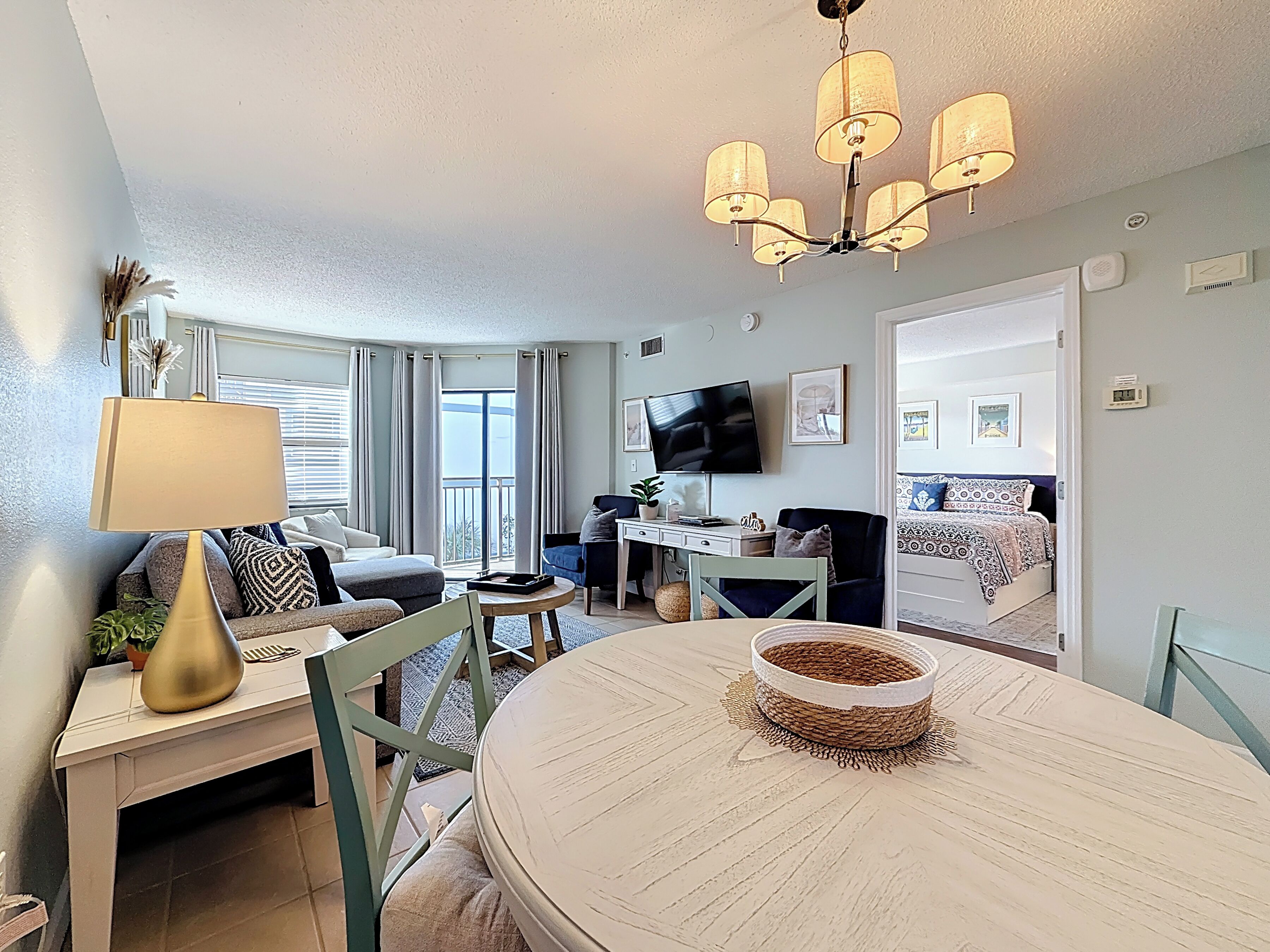 A well-lit living room with a dining area, a television, and a balcony with curtains.