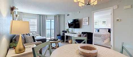 A well-lit living room with a dining area, a television, and a balcony with curtains.