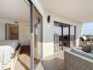 Ein Balkon mit Korbmöbeln, einer Schiebeglastür und Blick ins Freie.
