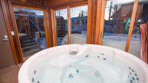 Un bain à remous avec une structure extérieure en bois et des portes en verre donnant sur un espace extérieur enneigé.