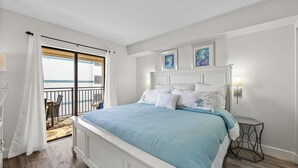 A bedroom with a large bed, a balcony with a view, and a small table with a lamp.