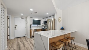 A modern kitchen with a marble island, stainless steel appliances, and wooden bar stools.