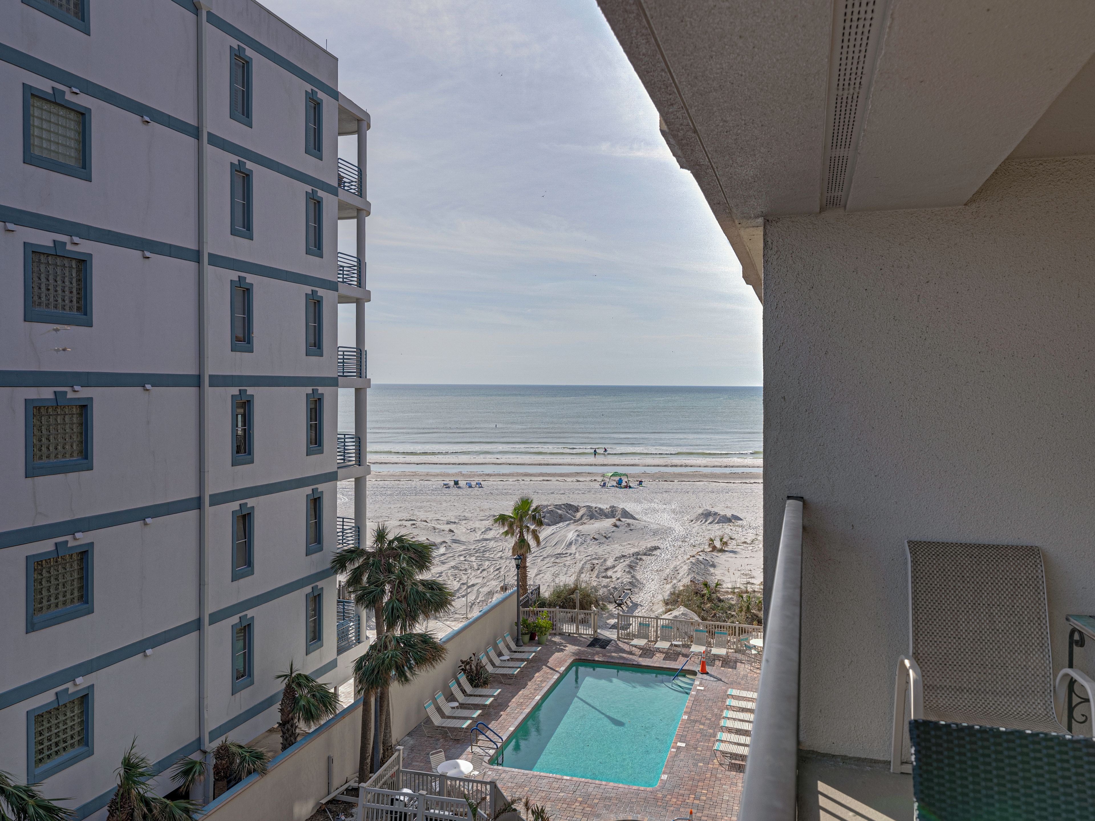 Un balcón de hotel con piscina, vista a la playa y sillones de descanso.