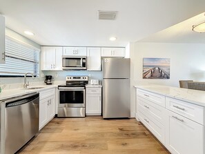 Une cuisine moderne avec des meubles blancs, des appareils électroménagers en acier inoxydable et un plancher en bois.