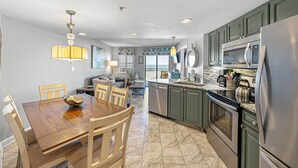 A modern kitchen with a dining area, granite countertops, stainless steel appliances, and a view to the outside. - Beachfront 2BR | Balcony, Pool & Spa (St. Pete Beach)