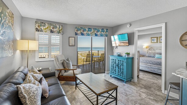 A living room with a sofa, a coffee table, and a TV mounted on the wall. There is a balcony with a view of the beach. - Beachfront 2BR | Balcony, Pool & Spa (St. Pete Beach)