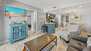A spacious living room with a wooden coffee table, a blue cabinet, and a striped sofa. - Beachfront 2BR | Balcony, Pool & Spa (St. Pete Beach)
