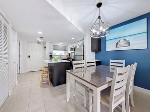 A modern kitchen with white cabinets, a black island, and a dining area with a wooden table and chairs.