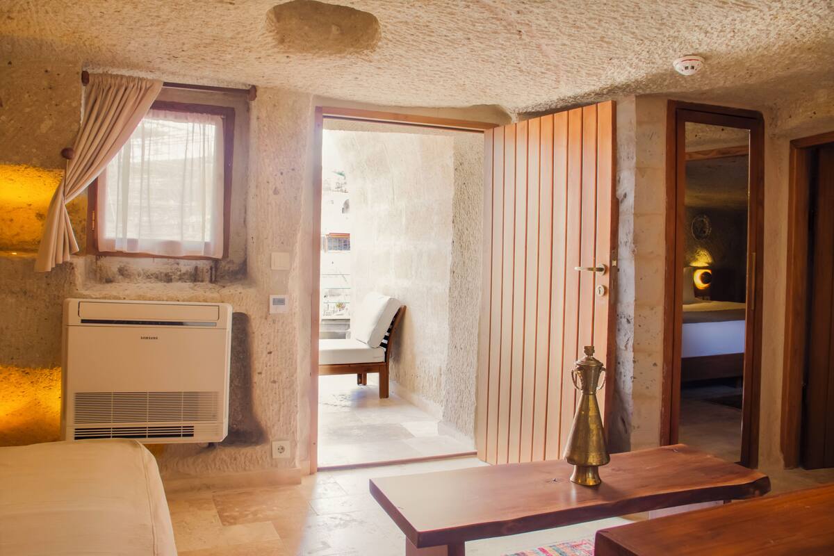 Una habitación con una cama, una mesa de madera, una ventana con cortinas, una puerta y un equipo de aire acondicionado.