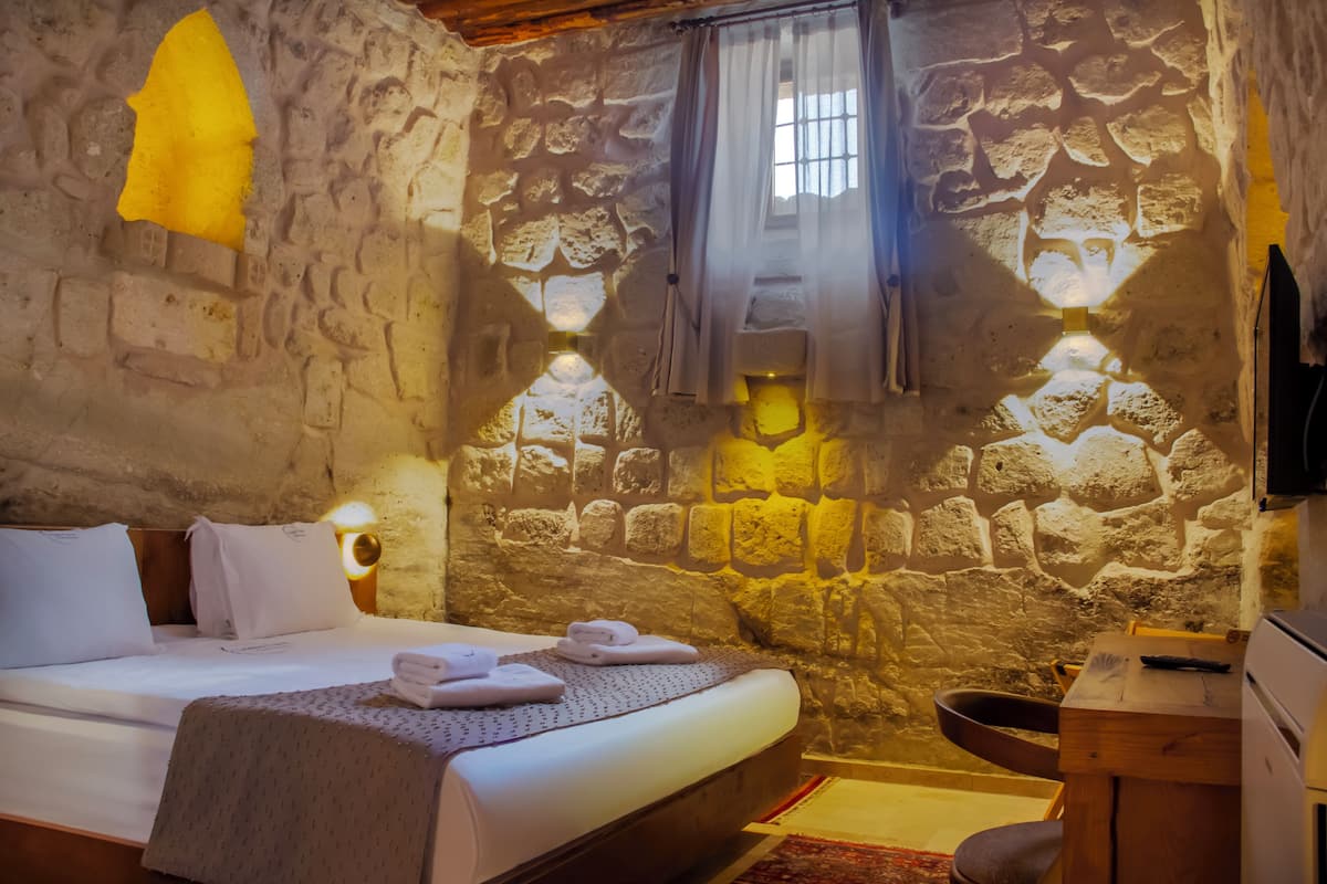 Habitación con paredes de piedra, una cama, una mesa y un lavamanos.