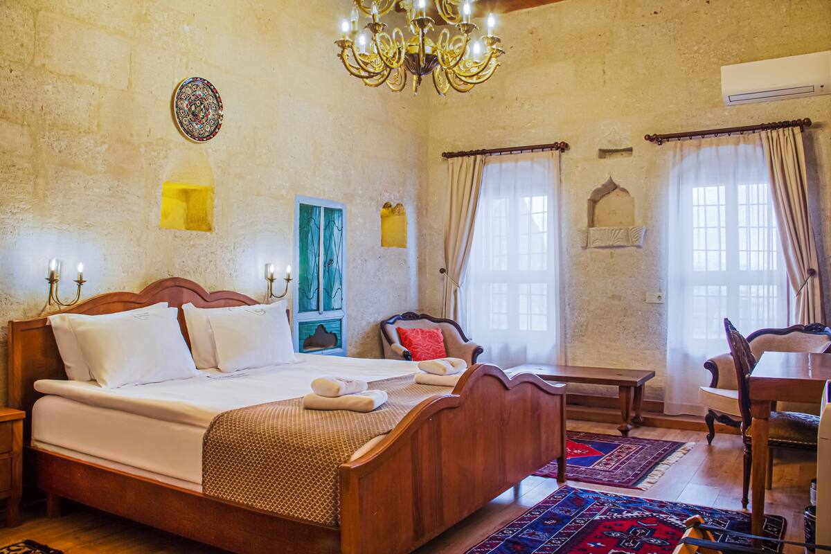 Una habitación tradicional con una cama de madera, un candelabro, una mesa de comedor y una alfombra estampada.