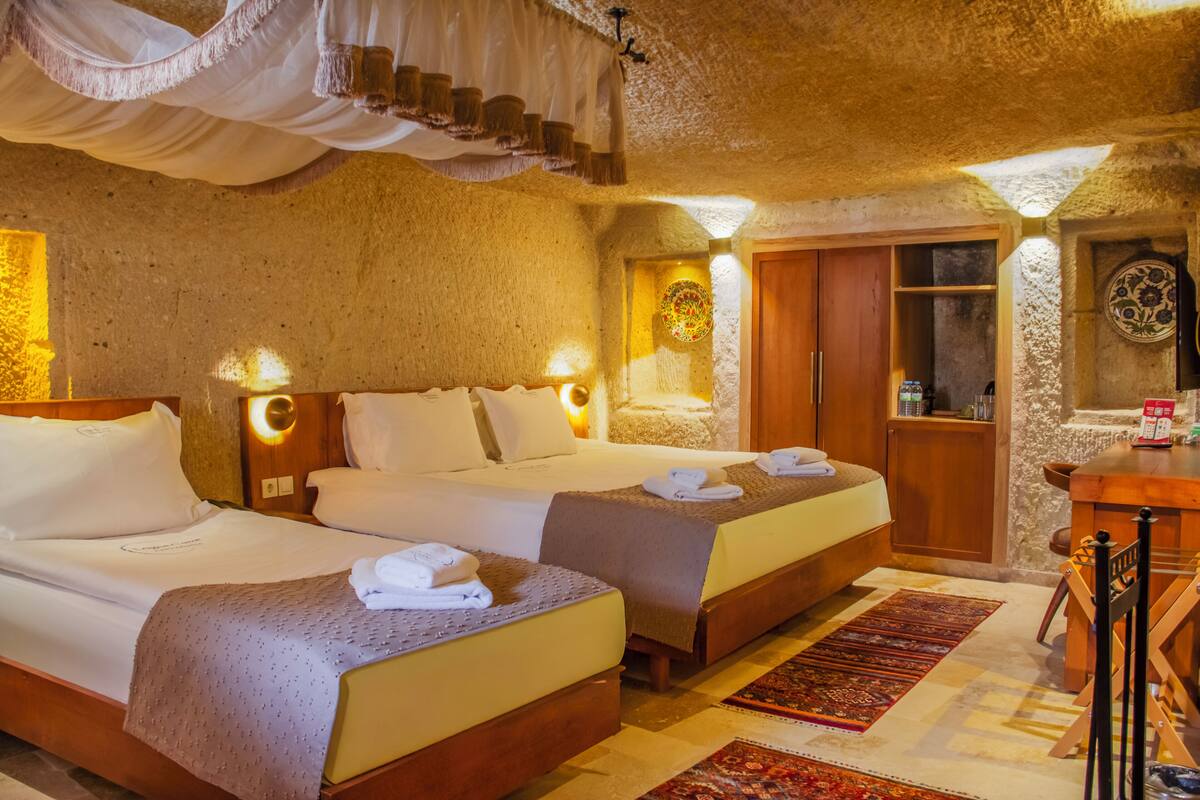 Una habitación con dos camas, un escritorio de madera, un espejo y una pared de piedra.