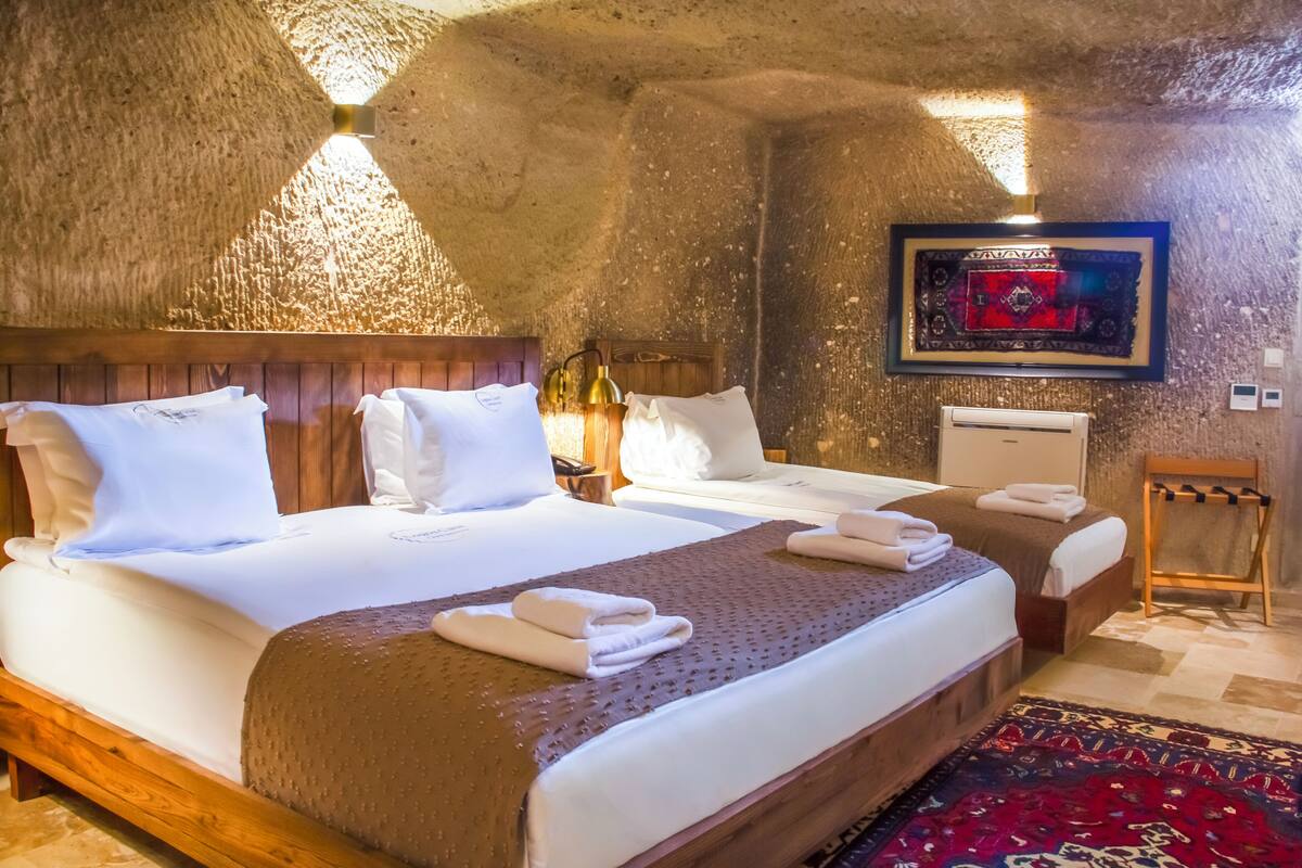 Una habitación con dos camas, cabeceros de madera, un televisor montado y un tapete rojo estampado.