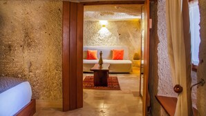 Une pièce avec un mur en pierre, une porte en bois, un lit, un canapé avec des coussins orange et une petite table avec une lampe.