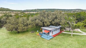 A small, single-story building with a flat roof, surrounded by a grassy field and dense trees.