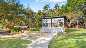 A small wooden structure labeled "Kitchen" with a concrete pathway leading to it, surrounded by trees and a well-maintained garden.