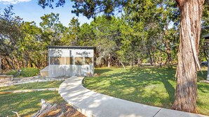 A small wooden cabin with a porch, surrounded by a well-maintained lawn and trees. - The Main House at Starlight Meadow (Wimberley)