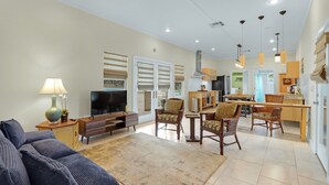 A spacious living area with a sofa, TV, and dining chairs. - The Main House at Starlight Meadow (Wimberley)