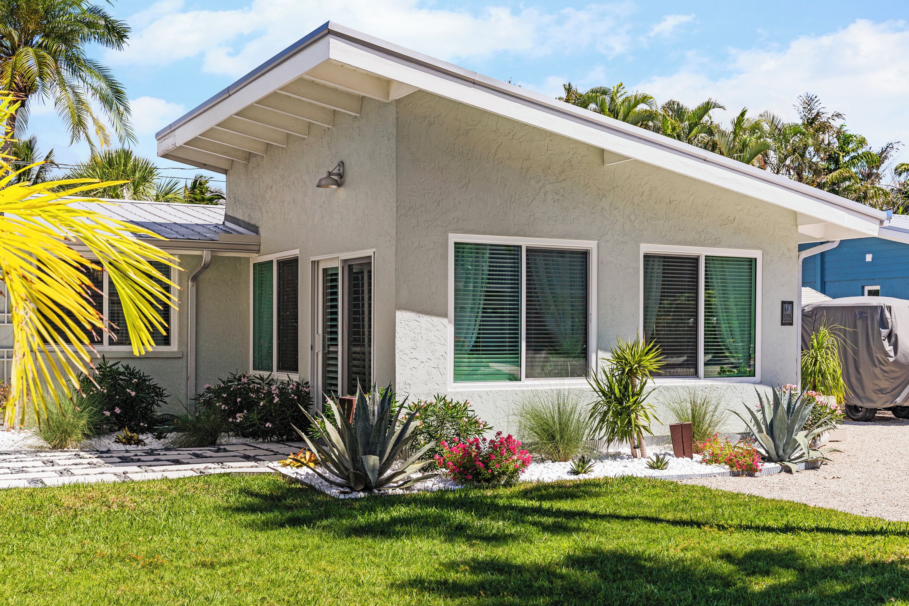 A modern house with a sloped roof, green shutters, and a well-maintained garden with various plants and flowers.