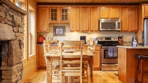 A kitchen with wooden cabinets, a stainless steel microwave, a stove, and a dining area with a wooden table and chairs. - Almond Joy Hideaway Luxury cabin, fire pit, Bryson City, Fontana Lake (Almond)